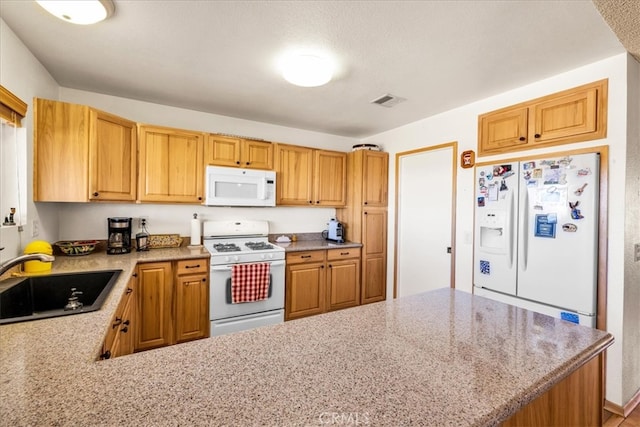 kitchen with visible vents, a sink, light stone counters, a peninsula, and white appliances