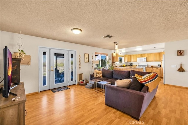 living area with a textured ceiling, visible vents, baseboards, and light wood-style floors