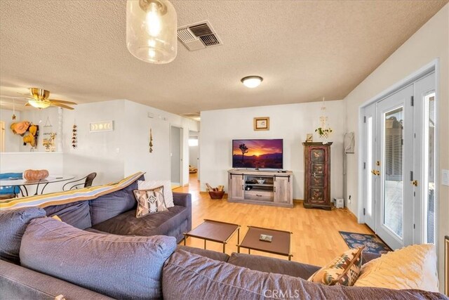 living room with light wood-style floors, a ceiling fan, a textured ceiling, and visible vents