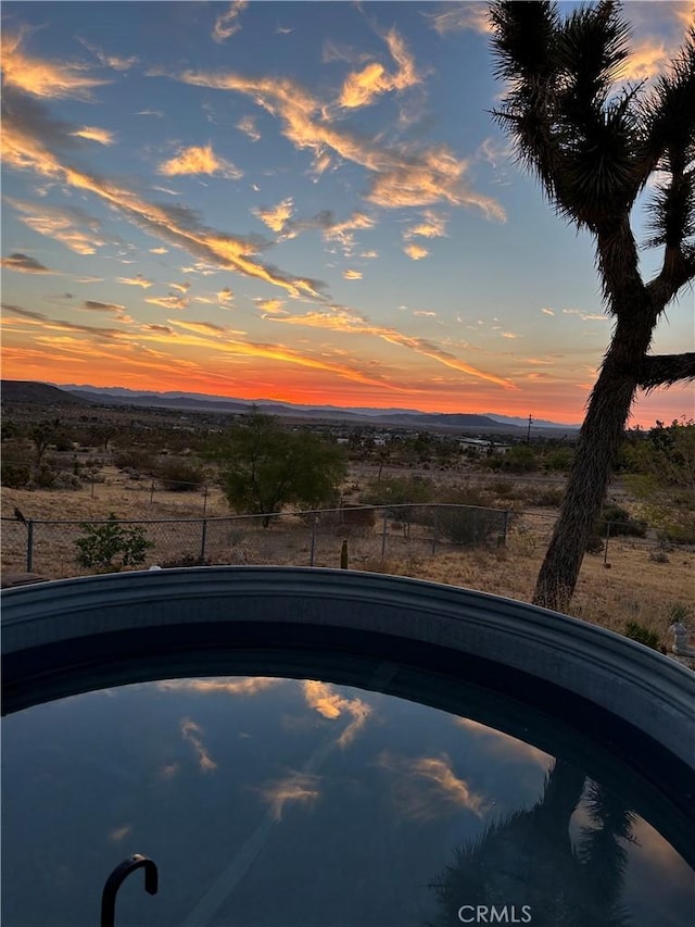 pool at dusk with fence, a rural view, and a pool