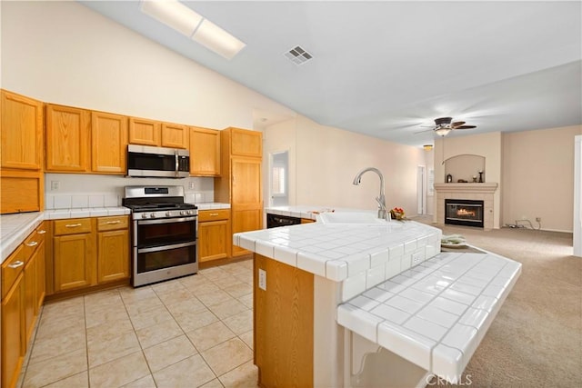 40949 Granite St, Palmdale, CA 93551 - kitchen with stainless steel appliances, tile counters, a ceiling fan, a tiled fireplace, and open floor plan