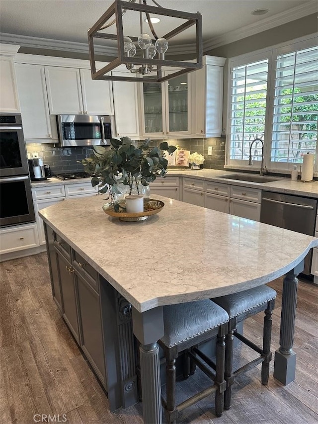 kitchen featuring appliances with stainless steel finishes, a sink, crown molding, and dark wood-style floors