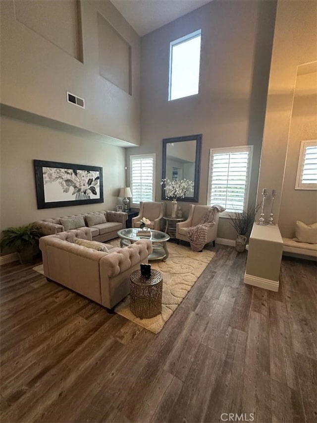 living room with baseboards, visible vents, wood-type flooring, and a towering ceiling