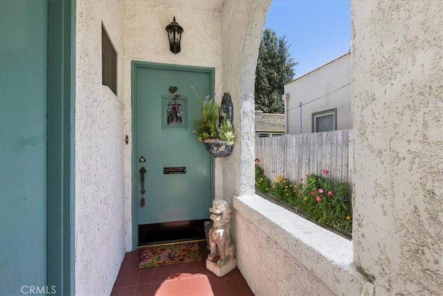 view of exterior entry featuring stucco siding and fence