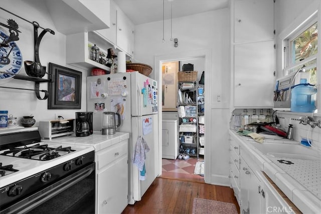 kitchen featuring white cabinets, tile counters, range with gas stovetop, washer / dryer, and dark wood-type flooring