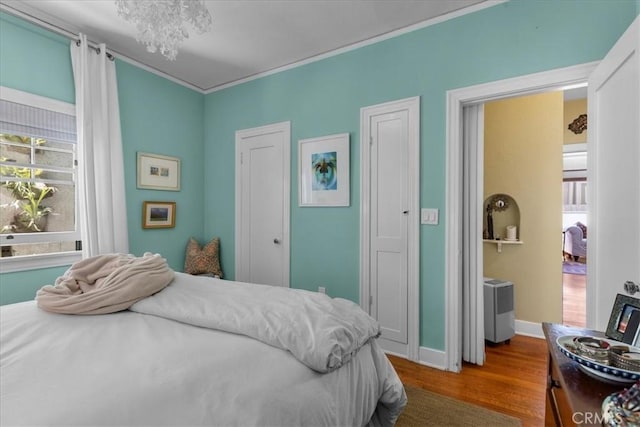 bedroom featuring baseboards, ornamental molding, multiple windows, and wood finished floors