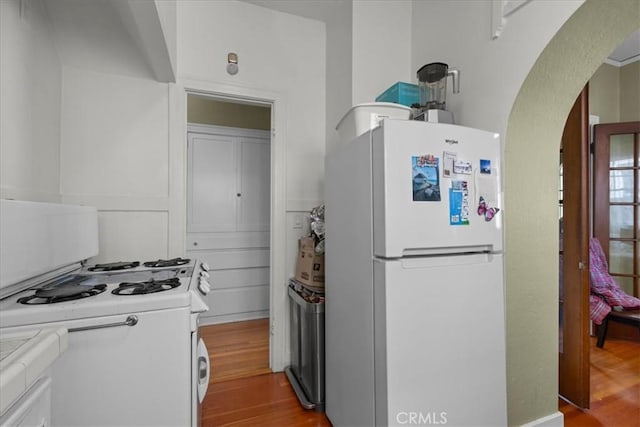 kitchen with white appliances, arched walkways, wood finished floors, and light countertops
