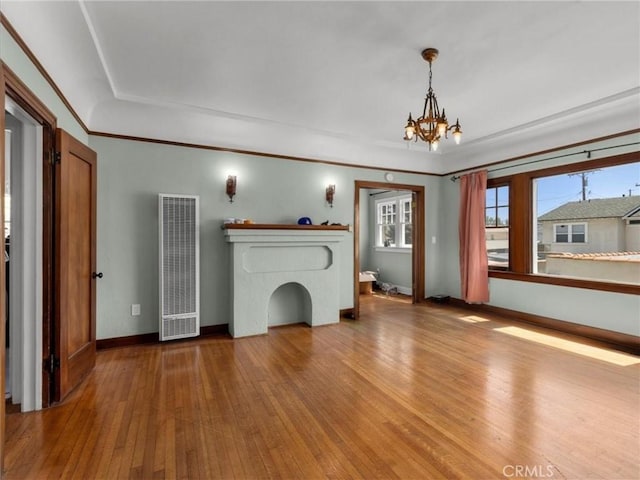 unfurnished living room featuring wood-type flooring, a heating unit, an inviting chandelier, and baseboards