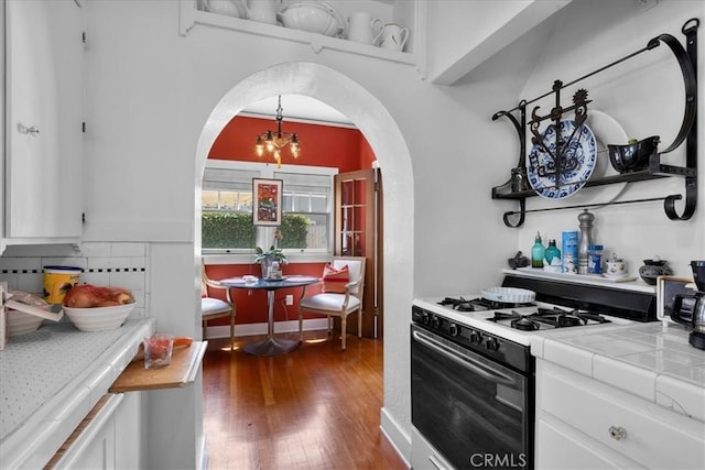 kitchen featuring wood finished floors, gas range oven, tile countertops, white cabinets, and arched walkways