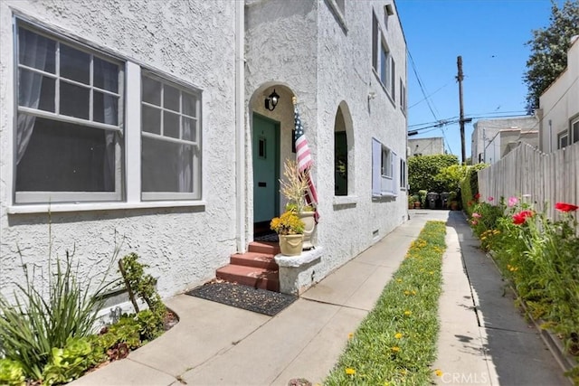 doorway to property featuring stucco siding and fence