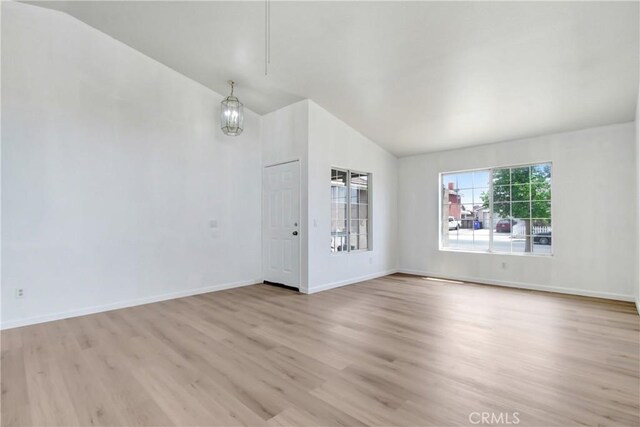 unfurnished living room with baseboards, light wood-style flooring, and lofted ceiling