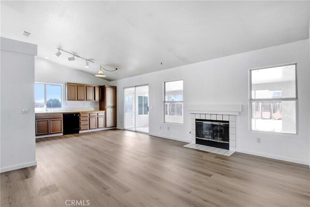 unfurnished living room with light wood-type flooring, baseboards, lofted ceiling, and a tiled fireplace
