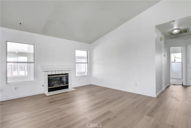 unfurnished living room with baseboards, vaulted ceiling, light wood finished floors, and a tile fireplace
