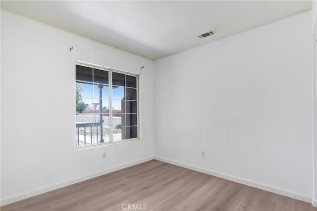 spare room with baseboards, wood finished floors, and visible vents