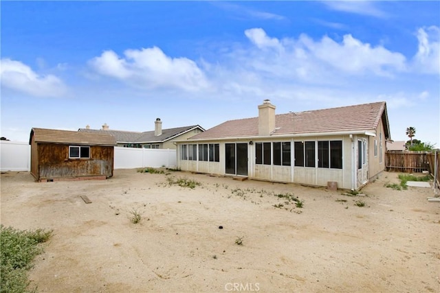 back of property featuring a fenced backyard, a shed, a chimney, a sunroom, and an outbuilding