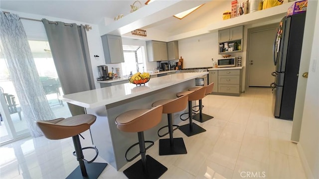 kitchen with light countertops, appliances with stainless steel finishes, gray cabinets, and a breakfast bar area