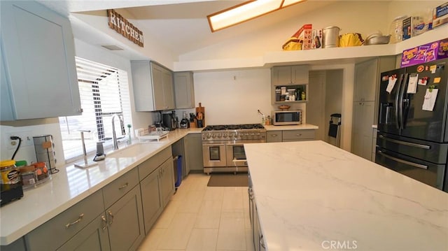 kitchen with gray cabinets, appliances with stainless steel finishes, light stone countertops, vaulted ceiling, and a sink