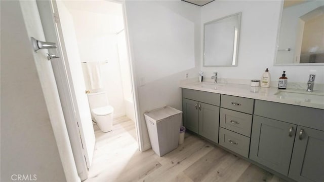 full bath featuring double vanity, toilet, a sink, and wood finished floors