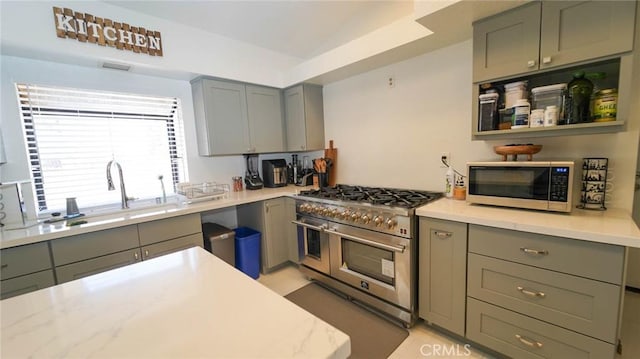 kitchen with light stone counters, a sink, gray cabinets, stainless steel appliances, and vaulted ceiling