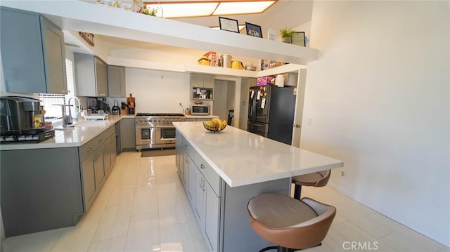 kitchen featuring gray cabinets, appliances with stainless steel finishes, a center island, a sink, and light countertops