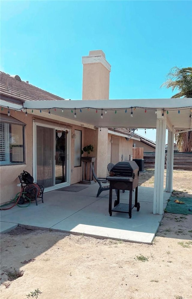 back of property featuring a patio, stucco siding, a chimney, and fence