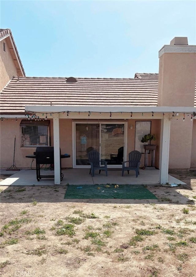 rear view of property featuring a tiled roof, a patio, and stucco siding