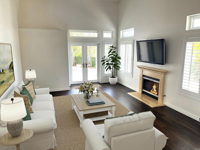 living room featuring baseboards, a towering ceiling, a glass covered fireplace, and wood finished floors