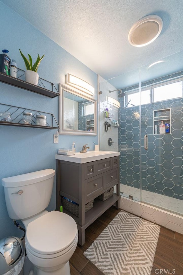 bathroom with toilet, wood finished floors, vanity, a textured ceiling, and a shower stall