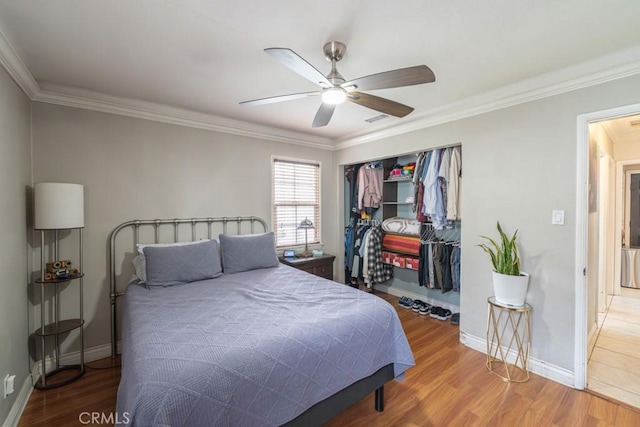 bedroom featuring a closet, wood finished floors, ornamental molding, ceiling fan, and baseboards