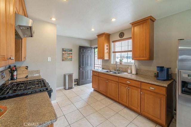 kitchen featuring brown cabinetry, light tile patterned floors, a sink, stainless steel fridge, and extractor fan