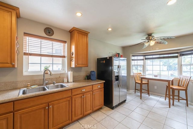 kitchen featuring a ceiling fan, a sink, brown cabinetry, a healthy amount of sunlight, and stainless steel refrigerator with ice dispenser