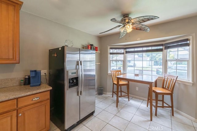 kitchen with a ceiling fan, brown cabinetry, stainless steel refrigerator with ice dispenser, light countertops, and light tile patterned flooring