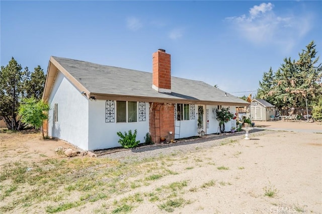 7120 Lyons Ave, Hesperia, CA 92345 - rear view of house featuring a storage unit, stucco siding, an outbuilding, and a chimney