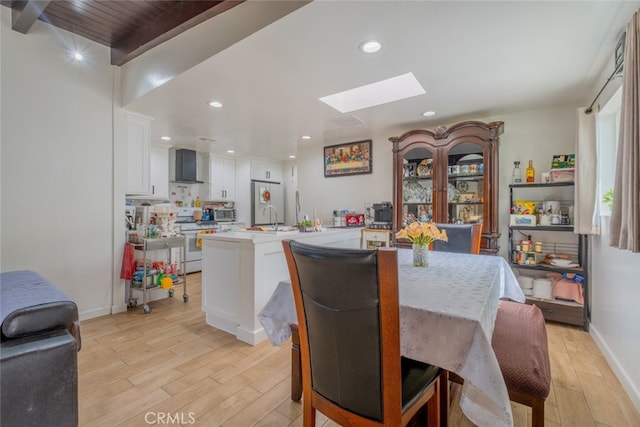 dining area with a skylight, light wood-type flooring, baseboards, beamed ceiling, and recessed lighting