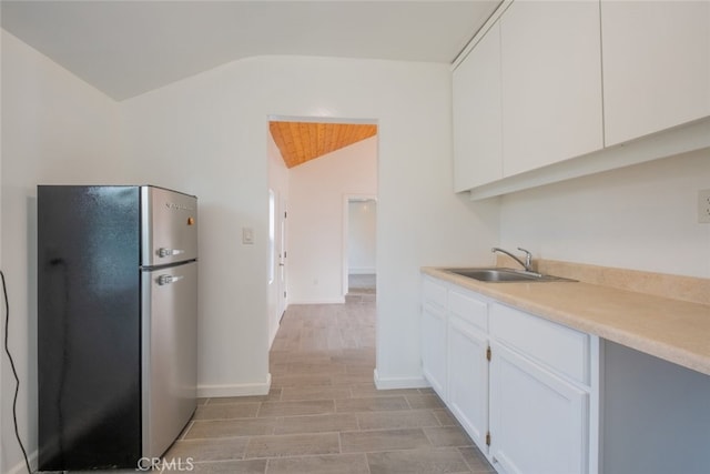 kitchen featuring a sink, light countertops, white cabinets, freestanding refrigerator, and lofted ceiling
