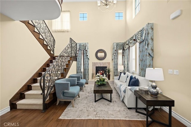 living room featuring an inviting chandelier, stairs, wood finished floors, a towering ceiling, and a lit fireplace