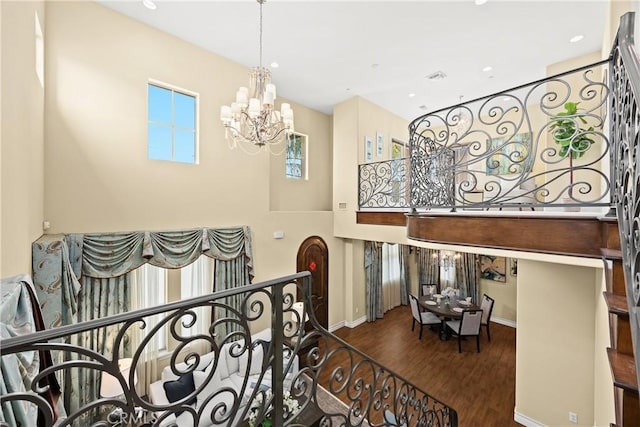 staircase featuring an inviting chandelier, a towering ceiling, wood finished floors, baseboards, and recessed lighting