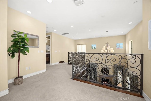 hallway with a chandelier, visible vents, baseboards, carpet floors, and an upstairs landing