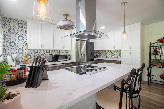 kitchen featuring island range hood, appliances with stainless steel finishes, light stone countertops, a peninsula, and white cabinetry