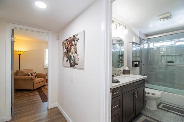 full bath with wood finished floors, vanity, baseboards, bath / shower combo with glass door, and toilet