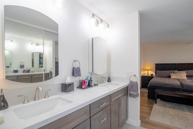 ensuite bathroom featuring double vanity, a sink, and wood finished floors