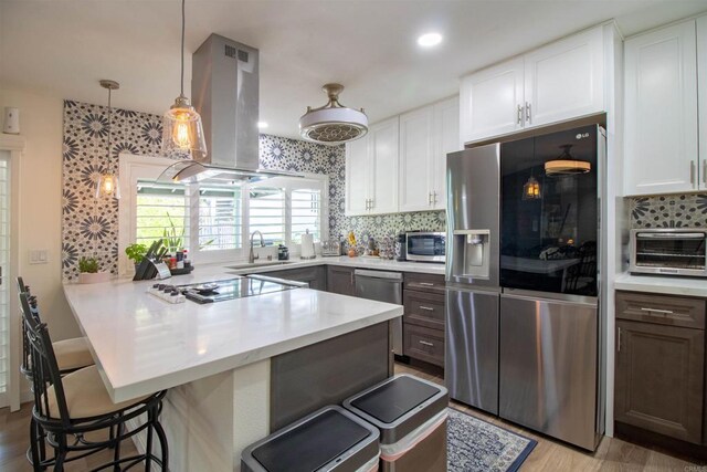 kitchen featuring a breakfast bar, stainless steel appliances, a peninsula, island exhaust hood, and a toaster