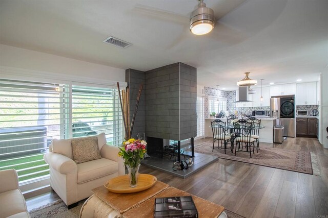 living area with visible vents, a multi sided fireplace, ceiling fan, and light wood-type flooring