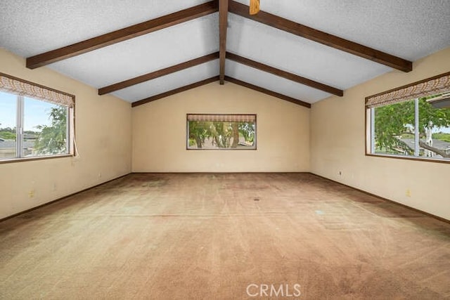 empty room featuring a healthy amount of sunlight, vaulted ceiling with beams, carpet, and a textured ceiling