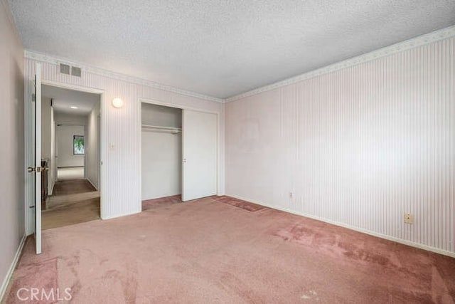unfurnished bedroom featuring carpet flooring, a textured ceiling, visible vents, and ornamental molding