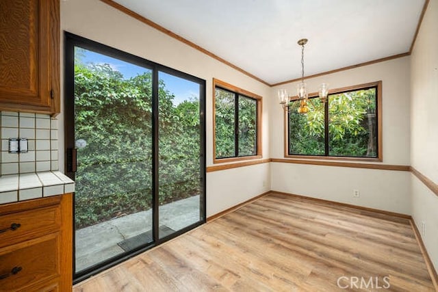 unfurnished dining area featuring an inviting chandelier, baseboards, ornamental molding, and light wood-style flooring