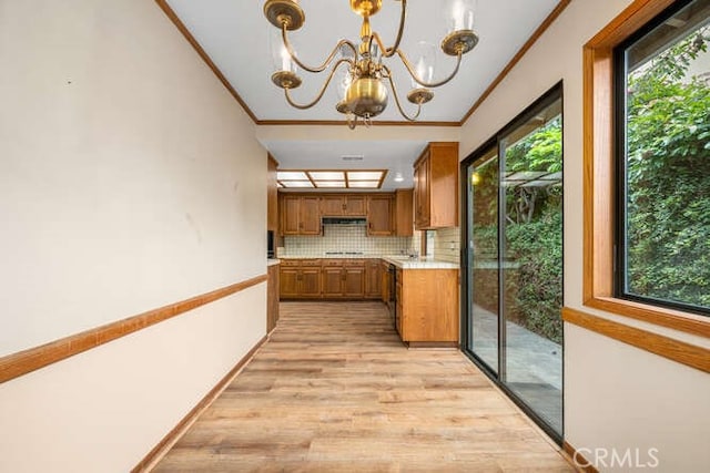 kitchen featuring brown cabinets, a notable chandelier, light countertops, light wood-type flooring, and ornamental molding