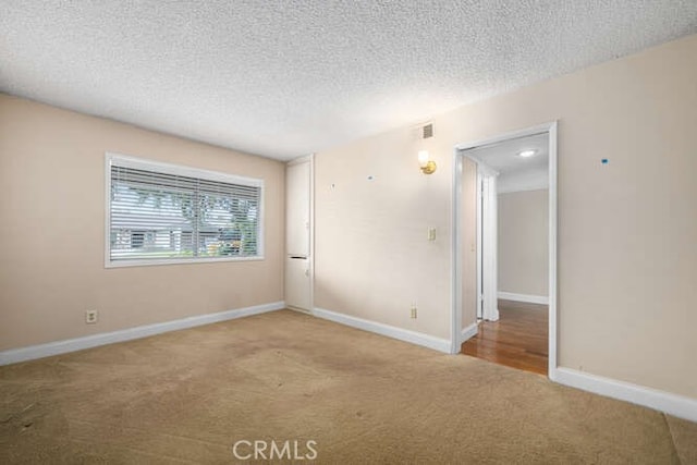 carpeted empty room featuring a textured ceiling, baseboards, and visible vents