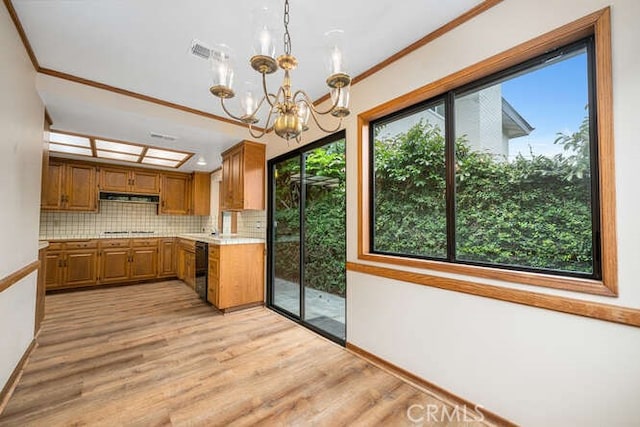 kitchen featuring brown cabinetry, light wood-style floors, light countertops, under cabinet range hood, and a chandelier