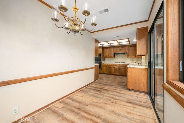 kitchen with brown cabinets, a chandelier, light wood-type flooring, under cabinet range hood, and visible vents